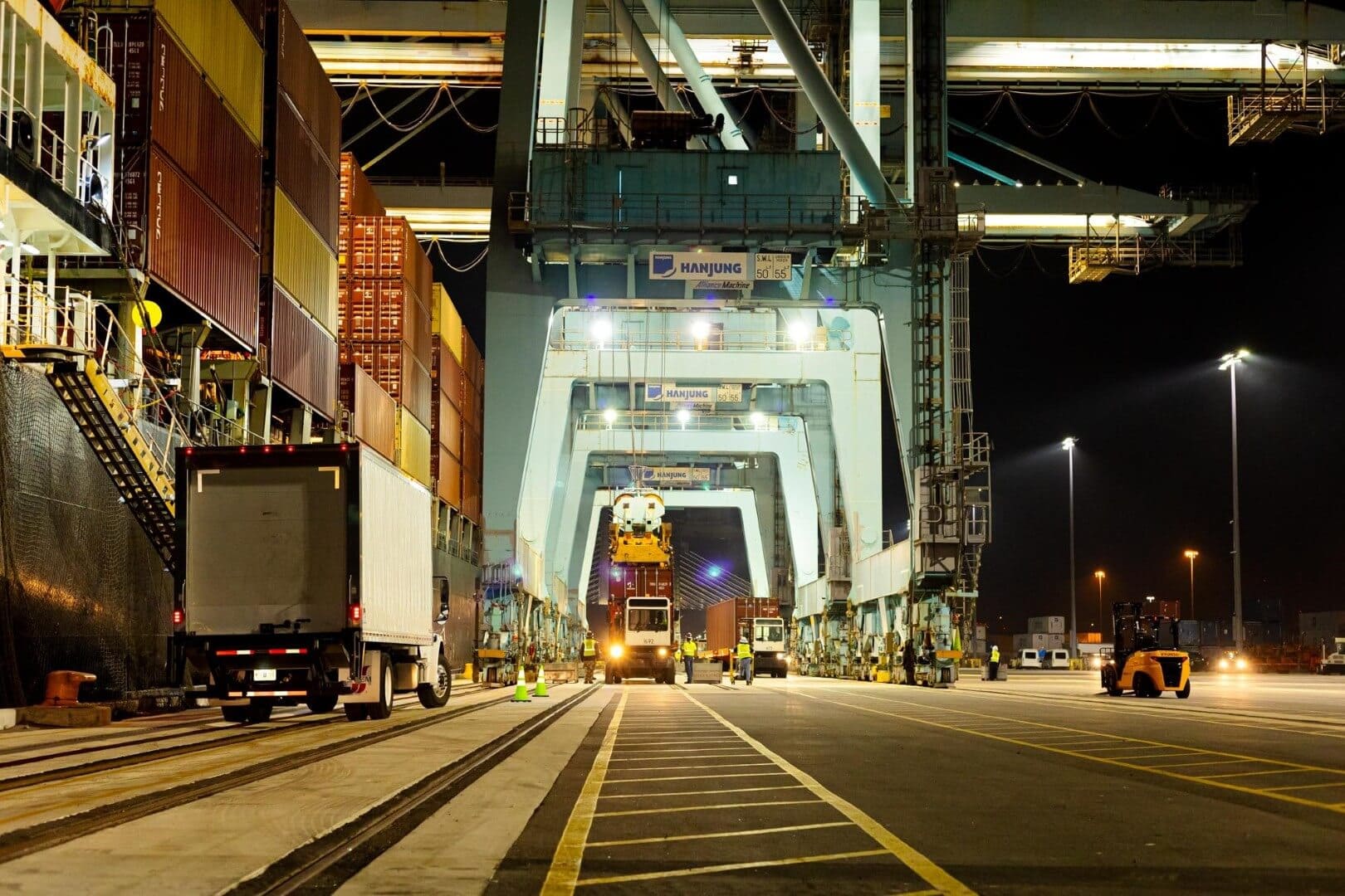 Loading dock at a busy port terminal with cargo containers and heavy machinery at night.