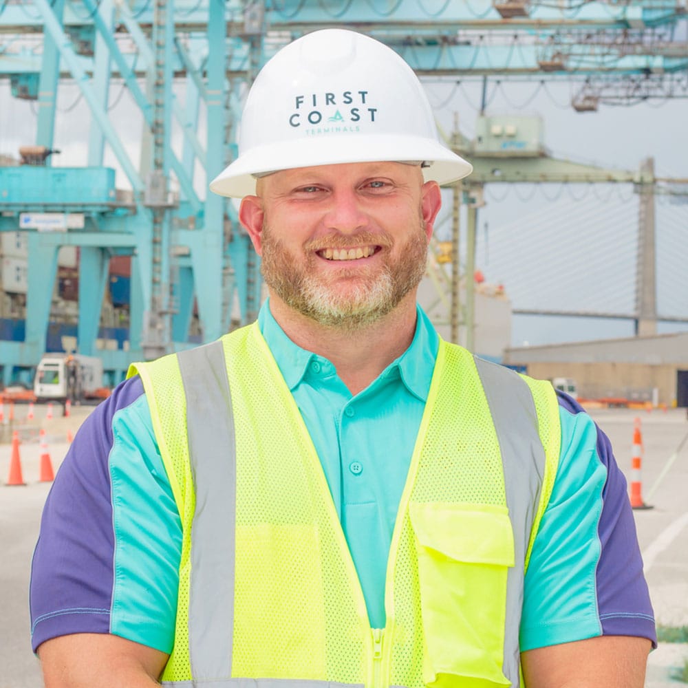 Brad Bishop wearing a safety helmet and vest at a busy port terminal.